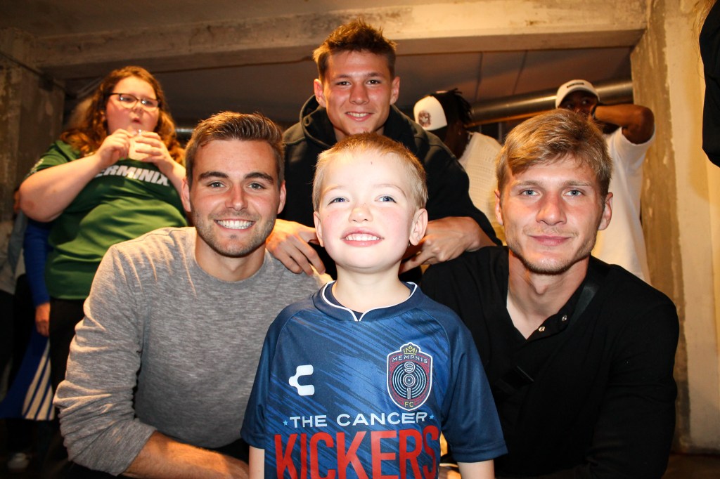 Carson Vom Steeg, Taylor Bailey and Nighte Pickering pose with a child in the new 901 FC jersey.